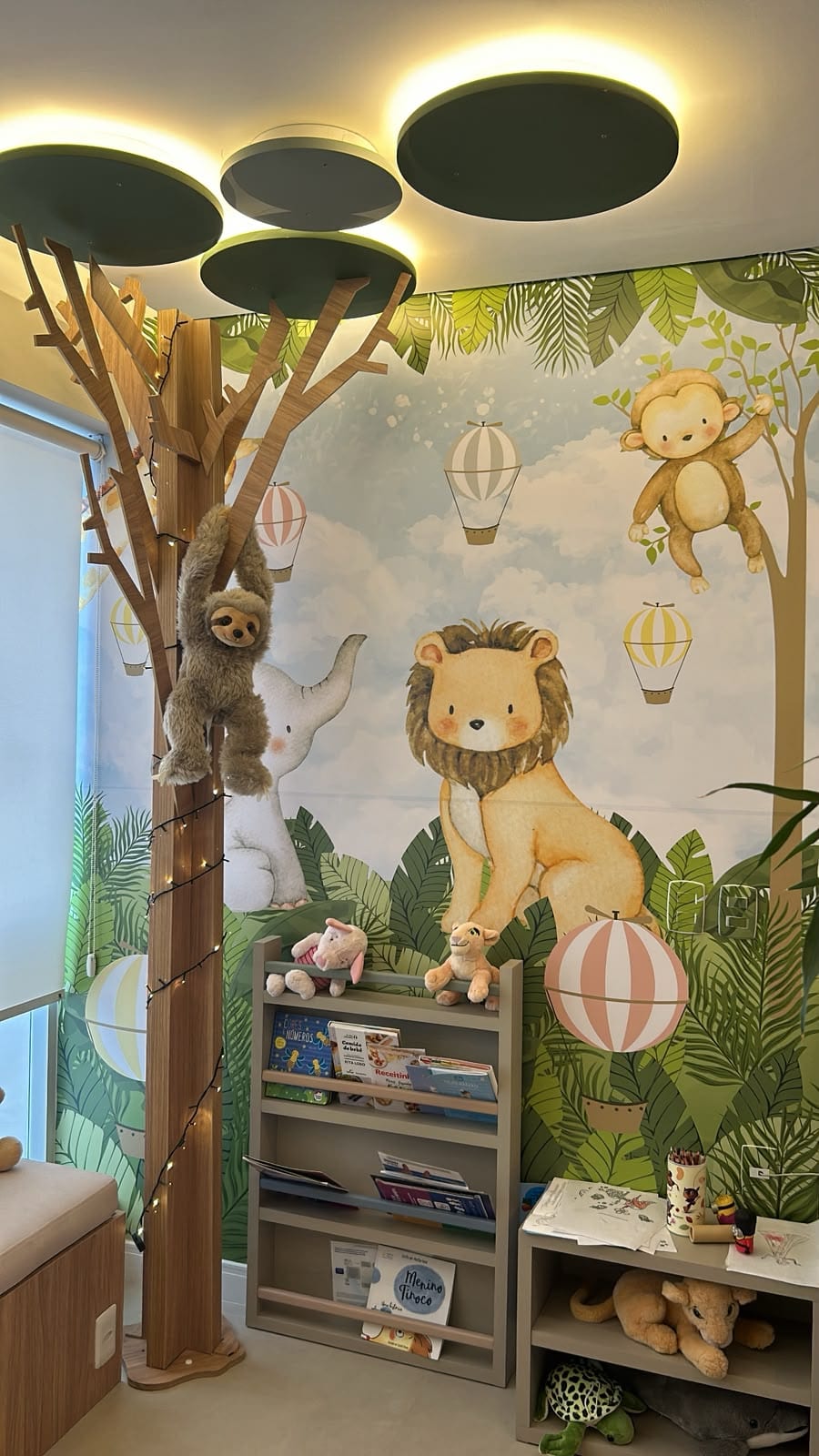 Espaço de leitura infantil com mural de leão, livros e bichos de pelúcia