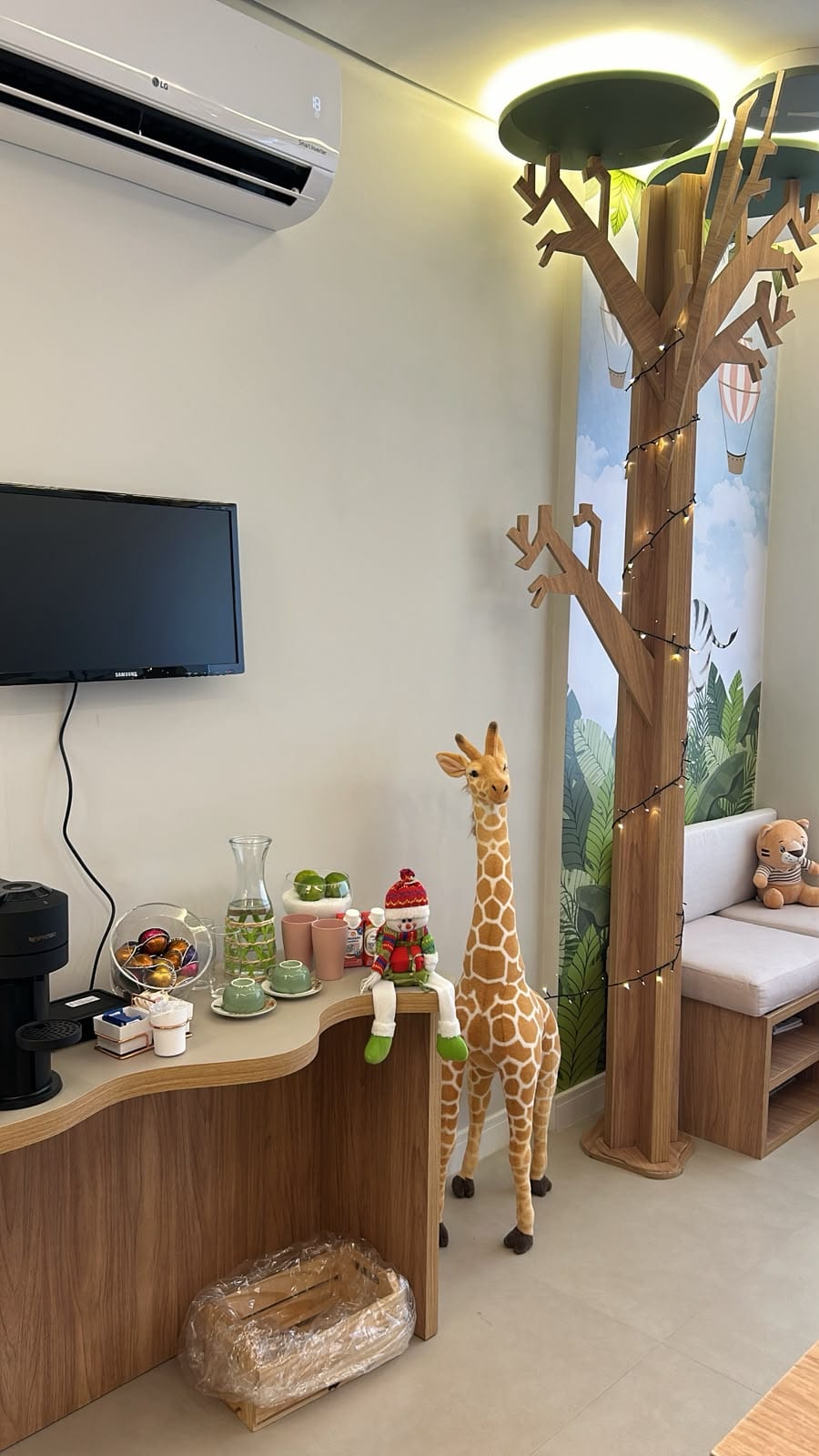 Estação de café e TV na sala de espera, com girafa de pelúcia